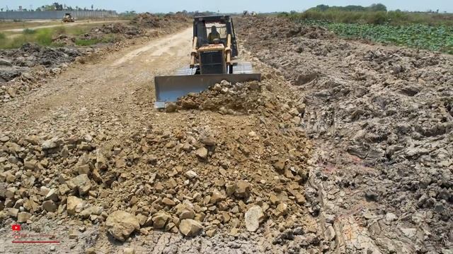Бульдозер KOMATSU толкает грунт и камень, создавая основание дороги в грязистой местности.