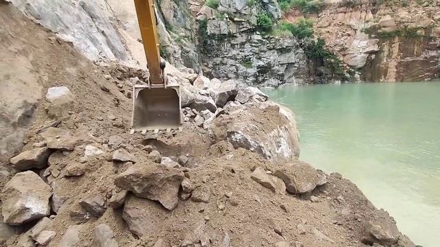 Экскаватор убирает большие камни бросая их в воду.