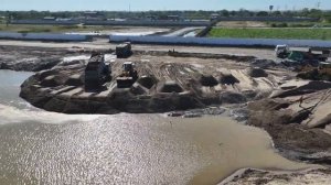 Бульдозер и колесный погрузчик с помощью 25-тонного самосвала засыпают озеро песком и камнем.