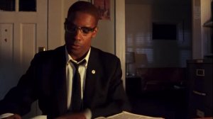 Дензел Вашингтон в черном костюме пиджаке белой рубашке в очках стучит по столу вырывает листок