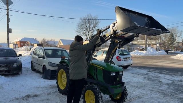 Минитрактор John Deere c погрузчиком чистит снег