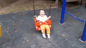Малыш весело качается на качелях На детской площадке Хохочет