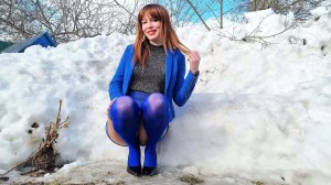 Рыжая длинноволосая девушка в синих нейлоновых чулках показывает новый синий наряд среди  сугробов