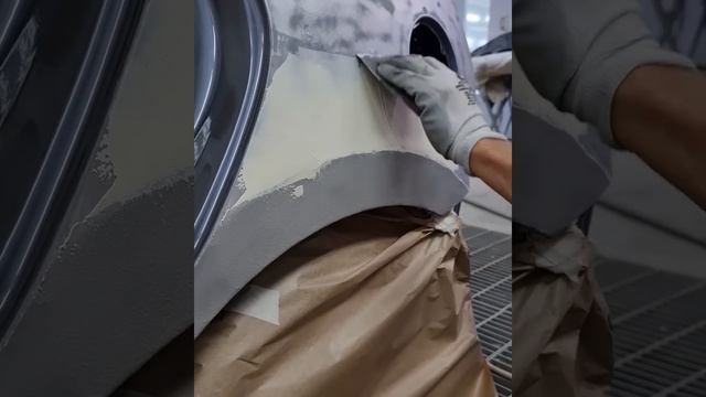 Маляр-подготовщик наносит 2 вида шпатлевки на рихтованное заднее крыло от автомобиля.