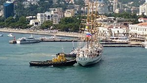 Трехмачтовый парусник заходит в порт, буксиры помогают швартоваться берегу