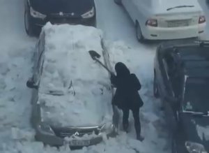 Девушка чистит снег с автомобиля железной лопатой
