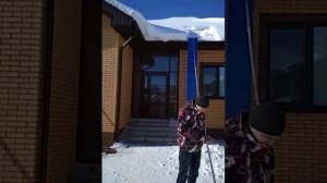 Чистка снега с крыши дома с помощью скребка для крыши с полотном