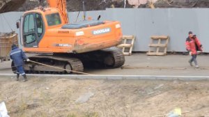 Экскаватору подкладывают под гусеницы доски, чтобы он мог доехать до входа стройки.