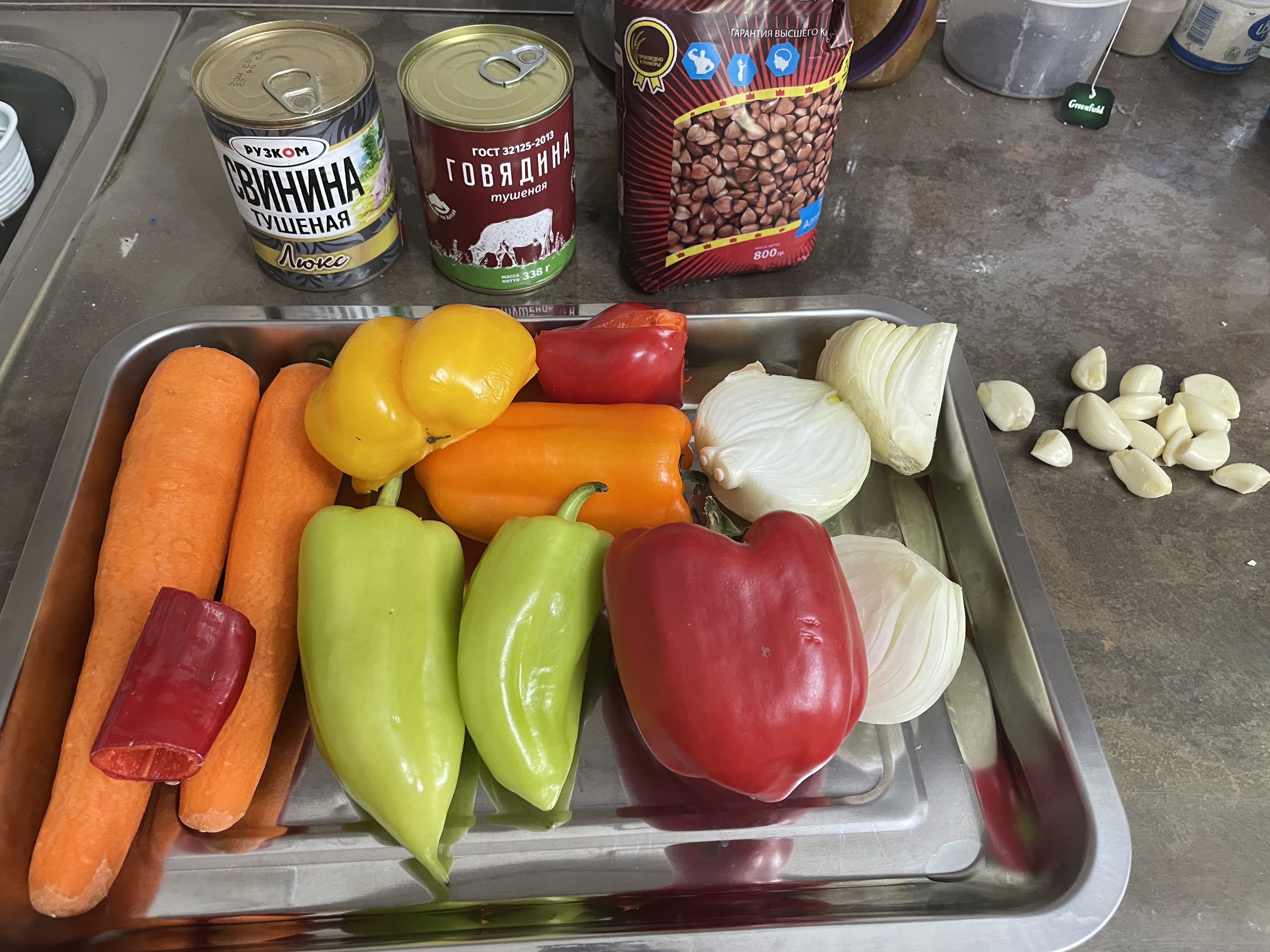 Тушёнка с гречкой и овощами в сотейнике на плите.