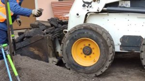 Боб Кэт у парадной забирает куски асфальта и перевозит их за дом, от туда возвращается со щебнем.