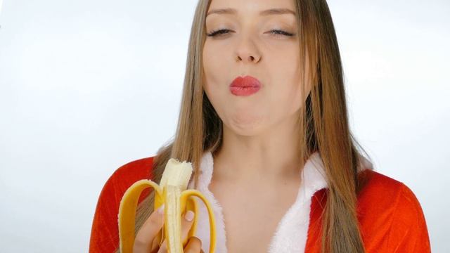 Молодая девушка в одежде снегурочки ест банан. A young girl dressed as a Snow Maiden eats a banana. смотреть онлайн