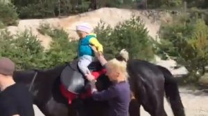 Маленькая 2-летняя девочка катается на лошади