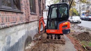 Миниэкскаватор копает траншею вплотную к стене