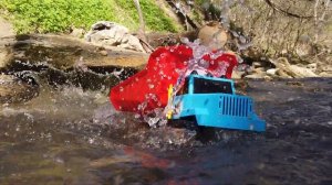 Трактор экскаватор помогает выехать из реки игрушечным машинкам. Грузовик застрял в грязи.