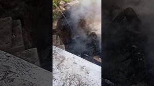 Ребёнок заливает водой горящие угли от костра в компостной яме.