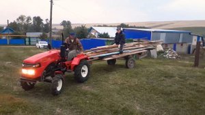 Русич-т18 в работе. Минитрактор перевозит длинные доски на самодельном прицепе.