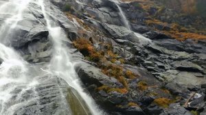 Вода падает со скалы вниз и бьется о камни.