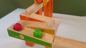 Большие шарики марблс катятся вниз по деревянной дорожке Один из шариков вкатывается в грузовик