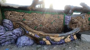 Цветник  у  забора.  дракон из  бетона  черновая  накидка.  парк.