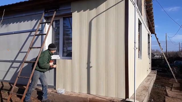 строители монтируют металлический сайдинг на фасад дома