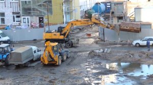Экскаватор выезжает со стройки, чтобы забрать помойный контейнер.