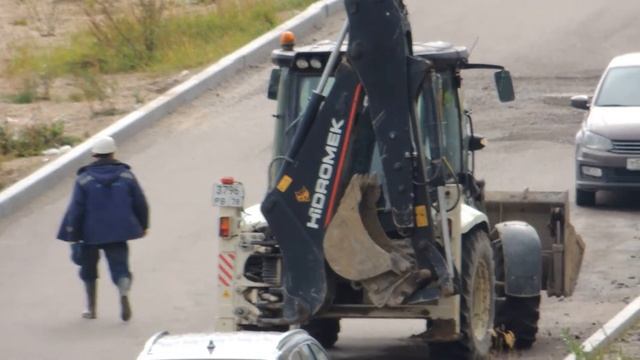 Трактор погрузчик едет, чтобы передвинуть крышку люка канализационную бетонную. смотреть онлайн