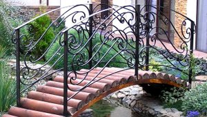 Декоративный ландшафтный мостик через ручей в саду на участке возле дома ковка