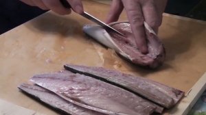 Пожилой мужчина у себя на кухне демонстрирует навыки разделки рыбы на филе.