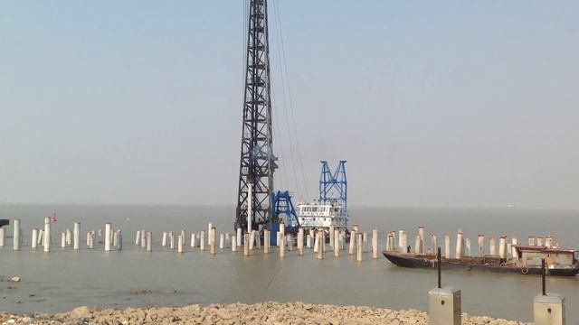 Забивка сваи оболочки дизель молотом. Сваебойная установка на палубе корабля.