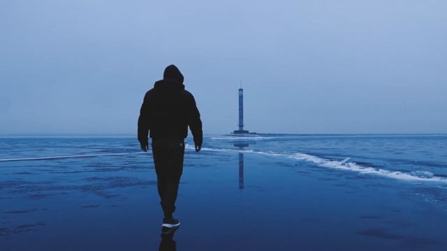 Идущий к маяку по льду человек. / A man walking towards the lighthouse on the ice.